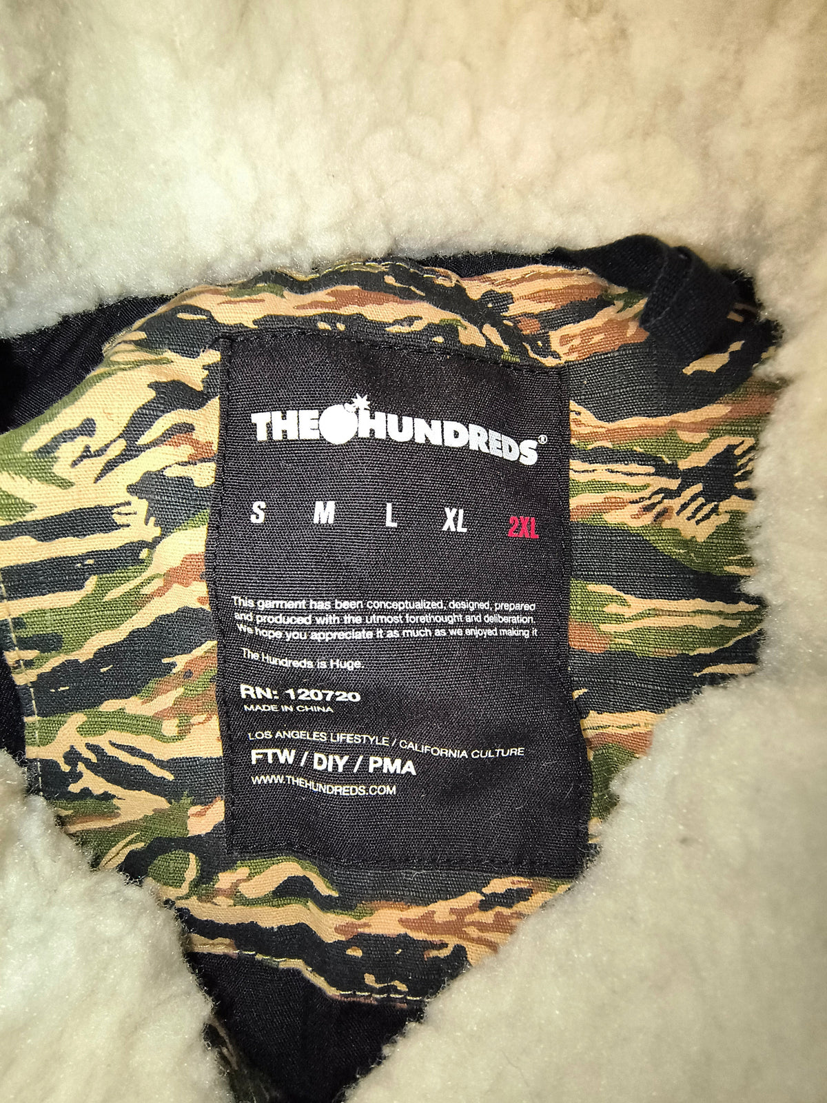 Awsum Thrift The Hundreds jacket size label showing 2XL on a tiger palms camouflage fabric background