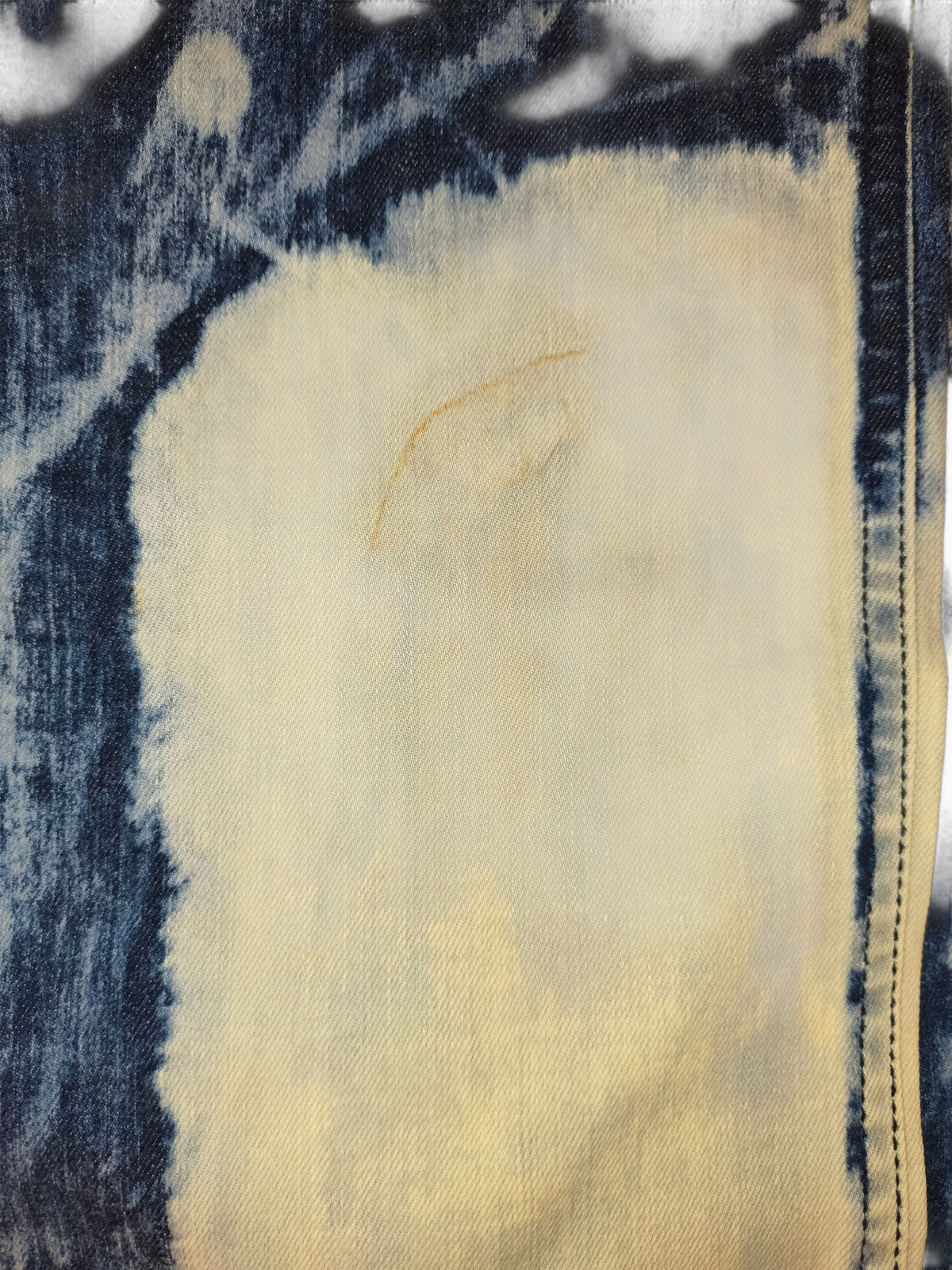 Awsum Thrift Golden Denim bleached indigo tie-dye jeans fabric detail showing a minor yellowish storage mark on thigh