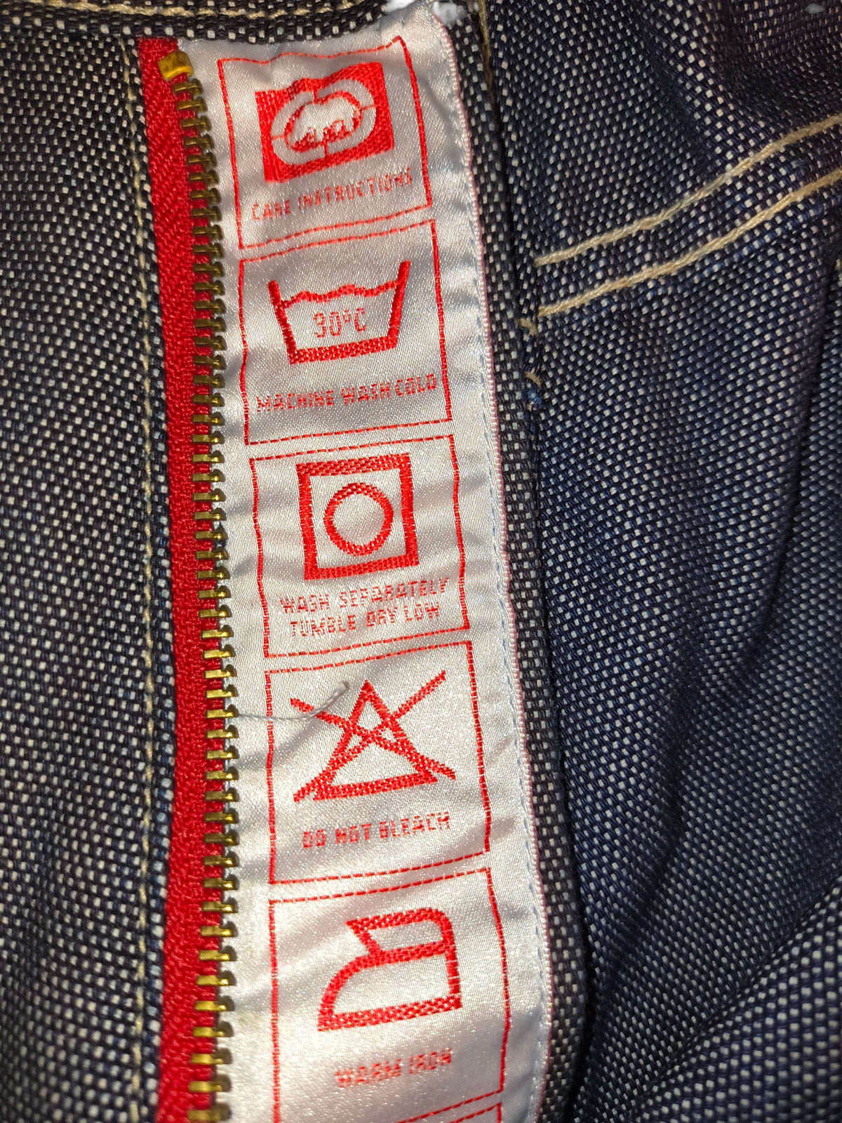 Awsum Thrift Marc Ecko vintage jeans care label with red icons on white fabric against dark indigo denim