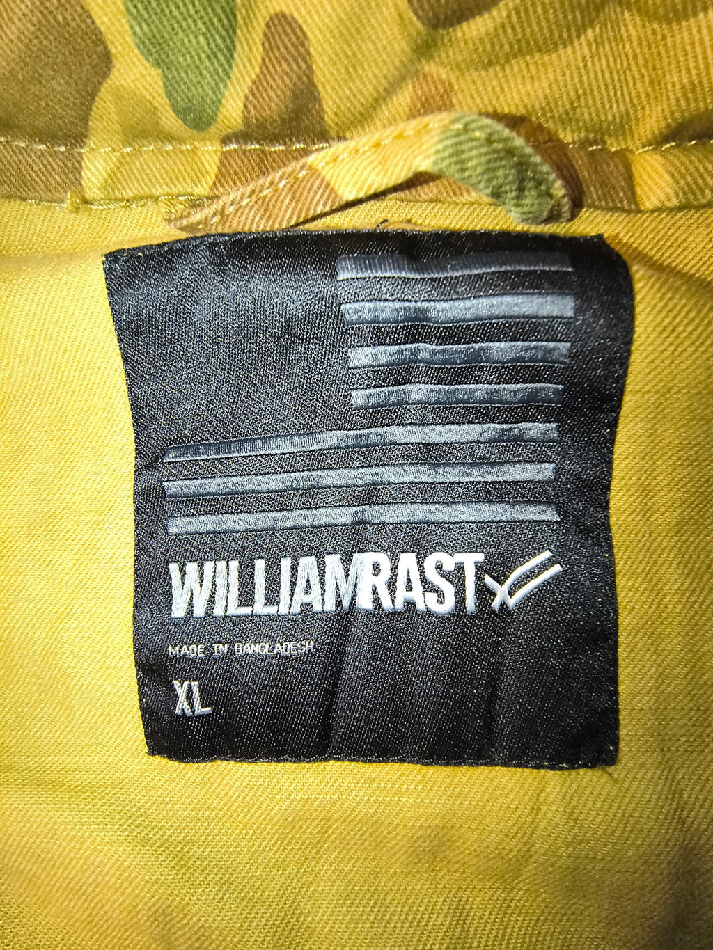 Awsum Thrift William Rast black fabric clothing label with American flag design and size XL on camo field jacket